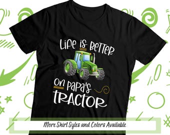 May include: A black short-sleeved t-shirt featuring a graphic of a green tractor. The text reads "Life is BETTER on papa's TRACTOR" in white and yellow lettering. The design is centered on the chest of the garment.