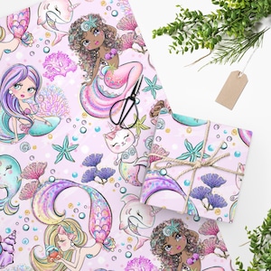 May include: Wrapping paper featuring a repeating pattern of mermaids, narwhals, and sea creatures on a light pink background. The design includes coral, starfish, and bubbles in shades of pink, purple, blue, and yellow. A pair of black scissors is present.