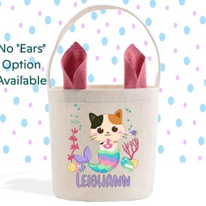 May include: A white canvas Easter basket with a mermaid cat design. The cat is wearing a purple seashell bra and has orange, black, and white fur. The basket has a pink fabric handle and the name "Leighaann" is printed on the front.
