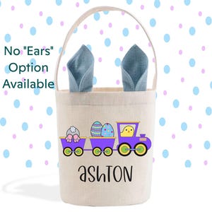 May include: A beige Easter basket with a train design featuring a bunny, Easter eggs, and a chick. The train is purple with yellow and green wheels. The name "Ashton" is printed in black script. The basket has blue bunny ears.