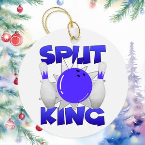 May include: A round white ceramic ornament featuring a blue bowling ball and two white bowling pins with blue accents. The text "SPLIT KING" is printed in bold blue letters above and below the graphic. A gold string is attached to the top.