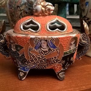 Könnte beinhalten: Ein Keramik-Räucherofen mit einem Deckel, der mit einem Herzmotiv verziert ist. Der Ofen ist mit komplizierten floralen und geometrischen Mustern in Gold-, Schwarz-, Rot- und Blautönen verziert.