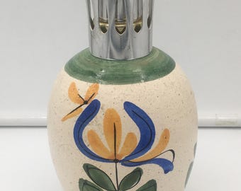 Könnte beinhalten: Dekorative Keramik-Duftlampe mit cremefarbenem Körper und silbernem Metallaufsatz. Die Lampe hat ein handgemaltes Blumendesign in Blau, Gelb und Grün. Die Lampe dient zur Verbreitung von Duftölen.