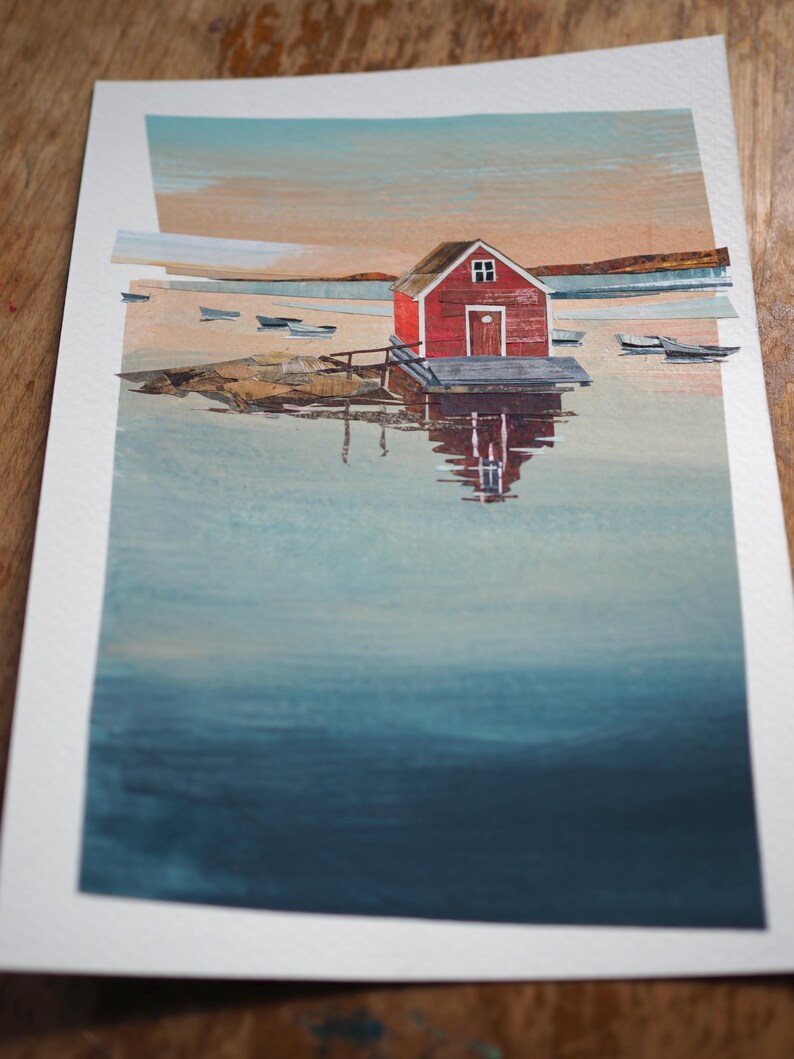 Puede incluir: Pintura a la acuarela de una caseta de botes roja en un muelle, reflejada en el agua. La obra representa una escena costera serena con peque&ntilde;as embarcaciones y una colorida puesta de sol. La pintura est&aacute; sobre papel blanco.