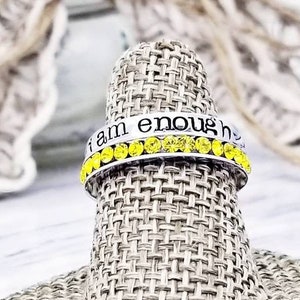 May include: A silver ring with yellow rhinestones and the words "I am enough" engraved on the band.