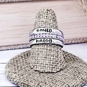 May include: Two silver rings with a row of small purple rhinestones. The top ring says "emily" and the bottom ring says "haley".