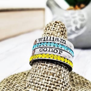 May include: Three silver rings with blue and yellow crystals. The rings are engraved with the names "William" and "Conor".