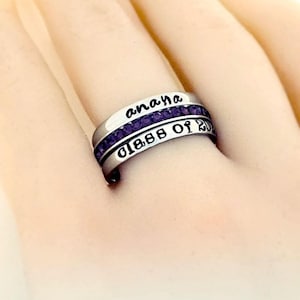 May include: A silver ring with purple gemstones and the inscription "anaya class of 202"