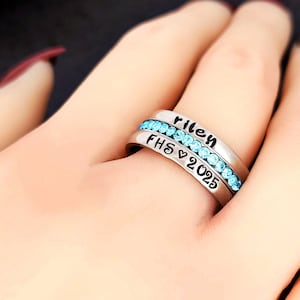 Könnte beinhalten: Zwei silberne Ringe mit blauen Edelsteinen. Der obere Ring sagt "Riley" und der untere Ring sagt "FHS 2025".
