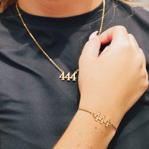 Op de afbeelding: Goudkleurige ketting- en armbandset. De ketting heeft het nummer "444" als hanger en de armband toont ook "444". Beide stukken zitten aan een delicate ketting, waardoor een minimalistische sieradenset ontstaat.