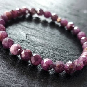 Puede incluir: Un brazalete de piedras preciosas rosas con cuentas facetadas. El brazalete está hecho de piedras naturales y está enhebrado en un cordón elástico transparente.
