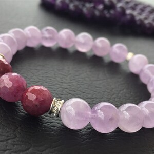 Pode incluir: Um bracelete de pedras preciosas roxo e rosa com um detalhe prateado. O bracelete é feito de contas redondas e tem uma mistura de contas roxas claras e escuras.