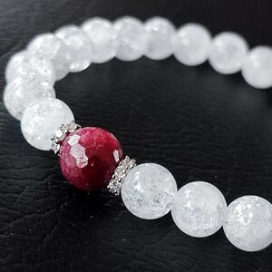 Puede incluir: Una pulsera de cuentas con cuentas de cuarzo blanco agrietado y una gema roja oscura facetada. La gema roja está acentuada con espaciadores plateados. La pulsera está ensartada en una banda elástica.