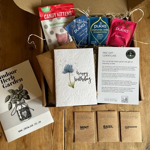 May include: A gift box filled with a variety of items, including a card that says "happy birthday", a small bag of sweets, tea bags, and seed packets for mint, basil, and coriander. The box also includes a certificate for planting a tree.