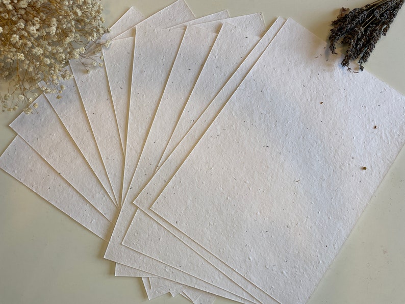 Może przedstawiać: Stos białych arkuszy papieru o spiekanej strukturze. Papier jest ręcznie robiony i ma naturalny, rustykalny wygląd.