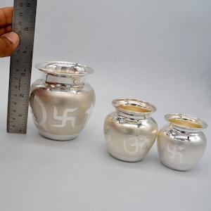 May include: Three silver-plated metal pots with intricate designs. The largest pot features a swastika symbol, the middle pot features an Om symbol, and the smallest pot features a swastika symbol.