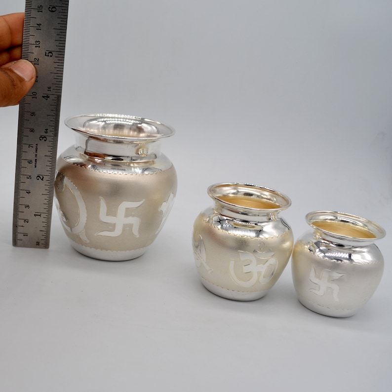 May include: Three silver-plated metal pots with intricate designs. The largest pot features a swastika symbol, the middle pot features an Om symbol, and the smallest pot features a swastika symbol.