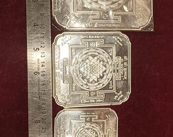 May include: Three silver-colored metal squares with intricate designs. Each square features a geometric pattern with a central star shape. The squares are arranged in descending size order, with the largest square at the top and the smallest square at the bottom.