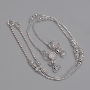May include: A pair of silver anklets with small beads and decorative charms. The anklets are made of a thin chain and have a delicate design.