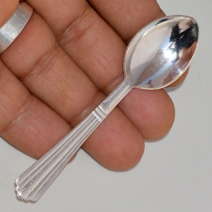 May include: A small, silver spoon with a fluted handle. The spoon is about 4 inches long and has a rounded bowl.