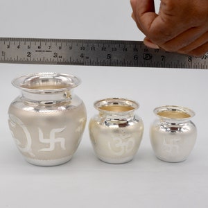 May include: Three silver pots with intricate designs. The largest pot is 4 inches tall and features a swastika symbol. The middle pot is 3 inches tall and features an Om symbol. The smallest pot is 2 inches tall and features a swastika symbol.