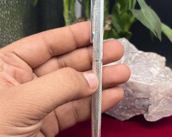 Puede incluir: Un bolígrafo de metal plateado con un cuerpo que presenta un patrón texturizado de diamantes entrecruzados. El bolígrafo incluye un clip de bolsillo recto integrado en la parte superior y una punta cónica lisa con acabado metálico.