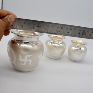 May include: Three silver pots with intricate designs. The largest pot is 3 1/4 inches tall and features a swastika symbol. The middle pot is 2 1/2 inches tall and features an Om symbol. The smallest pot is 1 3/4 inches tall and features a swastika symbol.