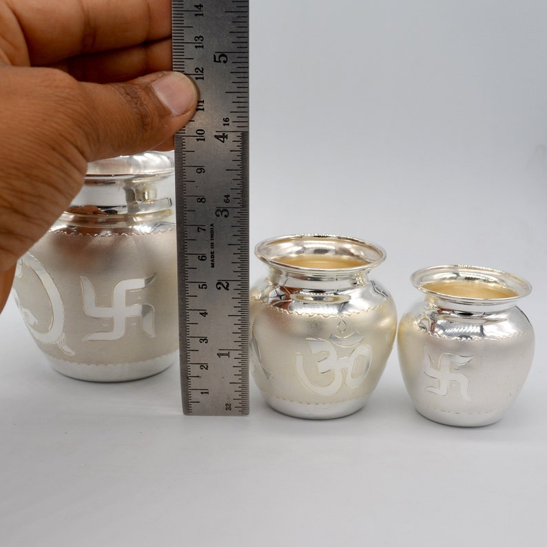 May include: Three silver pots with intricate designs. The largest pot is 4 inches tall and features a swastika symbol. The medium pot is 3 inches tall and features an Om symbol. The smallest pot is 2 inches tall and features a swastika symbol.