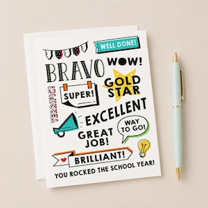May include: A white greetings card with the words "BRAVO", "SUPER!", "EXCELLENT", "GREAT JOB!", and "BRILLIANT!" in various fonts and colours. A light blue pen with a gold tip is on the right. The card says "YOU ROCKED THE SCHOOL YEAR!"