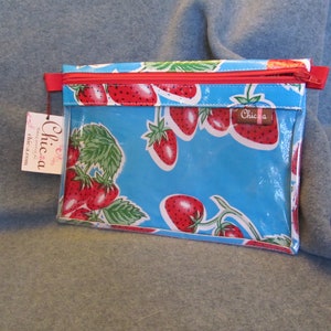 Puede incluir: Una bolsa azul con cremallera y un frente de vinilo transparente con un patr&oacute;n repetido de fresas rojas sobre un fondo blanco. La bolsa tiene una cremallera roja y una etiqueta blanca con la palabra "Chica" impresa en ella.