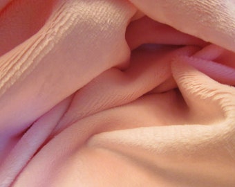 May include: Close-up of a soft, pink fabric with a fuzzy texture. The fabric is folded and draped, creating a smooth, flowing look.