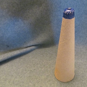 May include: A white ceramic cone with a blue top. The cone has a textured surface and is about 10 inches tall.