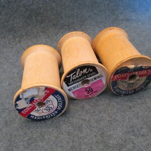 May include: Three wooden spools of thread with labels. The spools are labeled "Coats & Clark's", "Talon Dressmaker Spool Mercer Sewing", and "Coats & Clark's Mercerized Sewing".