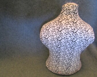 May include: A white decorative bust with a black line pattern. The bust has a rounded shape with a narrow neck and is set against a muted green background. The bust is a unique decorative item.