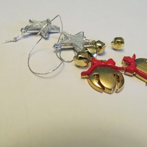 May include: A set of silver glitter star ornaments with a silver string and gold bells with red bows.