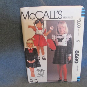 May include: McCall's sewing pattern featuring illustrations of little girls in dresses. The pattern cover shows a red dress, a black and white plaid dress, and the text "Ruffles & Lace for McCall's". The price is $3.00.