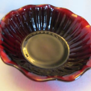 May include: A decorative, scalloped-edge bowl with a deep red exterior and a gold-colored interior. The bowl has a ridged design radiating from the center. The rim is edged with gold. This bowl is suitable for serving or display.