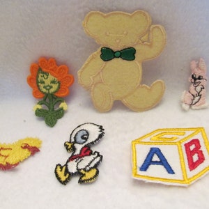 May include: A set of seven embroidered iron-on patches featuring a yellow chick, a white duck, a pink bunny, a yellow flower, a brown bear wearing a green bow tie, and a yellow block with the letters A and B in blue and red.