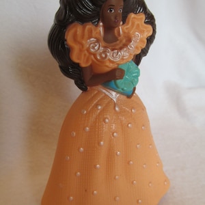 May include: A plastic doll with brown hair and a peach-colored dress with white polka dots. She is holding a blue flower in her hand.