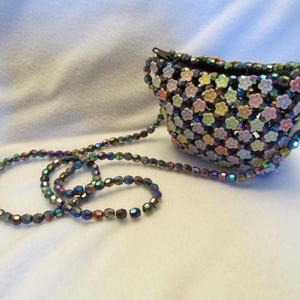 May include: A small, beaded purse with a shoulder strap. The purse is covered in small, colorful flower-shaped beads. The strap is made of iridescent beads. The purse has a black zipper and a black interior.