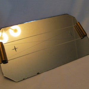 May include: A rectangular mirrored tray with gold metal handles. The tray has a beveled edge and a decorative etched design.