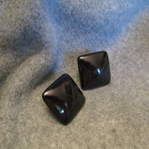 May include: A pair of black square-shaped earrings. The earrings are made of a glossy material.