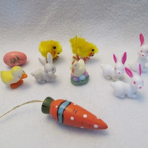 May include: A collection of Easter-themed decorations, including a yellow chick, a pink egg, a duck, a carrot, and several white bunnies with pink ears.