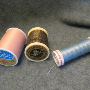 May include: Three spools of thread. One is pink and says "Coats Dual Duty Plus". One is gold and says "Antique Gold Thread". One is blue and says " Gütermann 100/3".