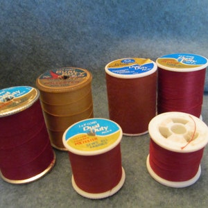 May include: Six spools of red thread, some with white and blue labels that say "Dual Duty" and "100% Polyester".