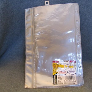 May include: Clear plastic pocket with a zipper closure and six holes for a binder. The pocket has a label on the back that says "FISKARS" and "Stuff Keeper Expanding File - 100% Service Promise".
