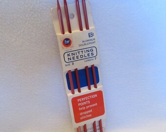 May include: A package of red aluminum double-point knitting needles. The package reads "KNITTING NEEDLES SIZE 3 LENGTH 7" and "PERFECTION POINTS help prevent dropped stitches."