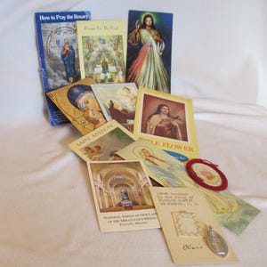 May include: A collection of religious cards and prayer books featuring images of saints, the Virgin Mary, and Jesus Christ. The cards are printed on paper and have a vintage look. The cards are arranged on a white surface. The text on the cards includes "How to Pray the Rosary", "Pray for the Dead", "Saint Anthony", "Little Flower", "National Shrine of Our Lady of the Miraculous Medal", and "To the Shrine of the Blessed Virgin Mary of Porris, O.P."