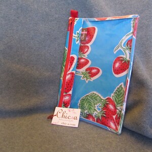 Puede incluir: Una bolsa de pl&aacute;stico transparente con cremallera roja y fondo azul. La bolsa est&aacute; decorada con un patr&oacute;n de fresas rojas sobre enredaderas verdes. La bolsa tiene una peque&ntilde;a etiqueta blanca con el texto "Chic-a" y una direcci&oacute;n de sitio web.