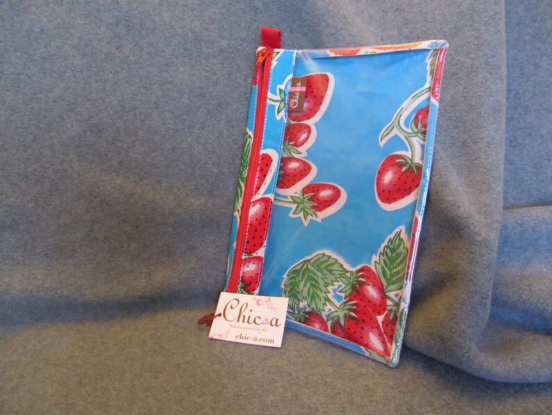 Puede incluir: Una bolsa de pl&aacute;stico transparente con cremallera roja y fondo azul. La bolsa est&aacute; decorada con un patr&oacute;n de fresas rojas sobre enredaderas verdes. La bolsa tiene una peque&ntilde;a etiqueta blanca con el texto "Chic-a" y una direcci&oacute;n de sitio web.